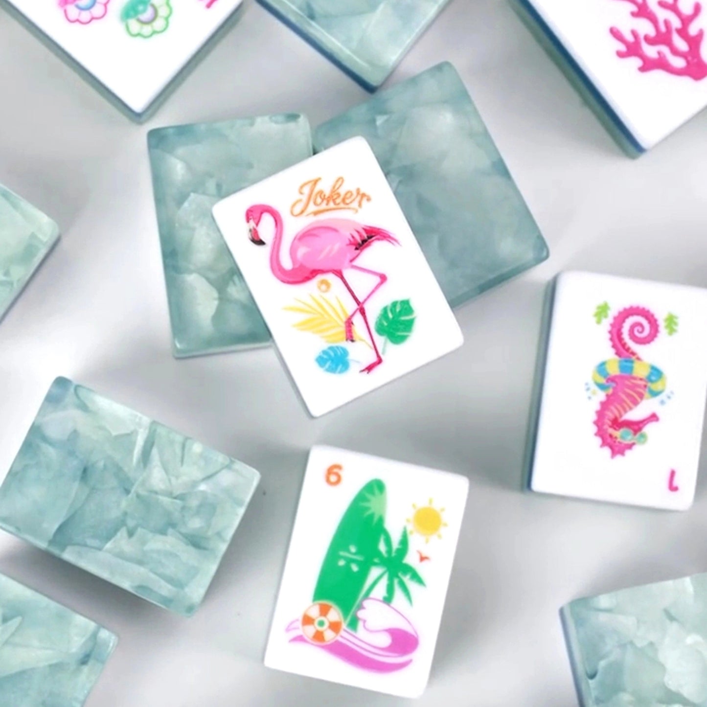 Coastal Breeze mahjong tiles close-up: pink flamingo joker, seahorse, surfboard and coral tiles with sea-glass aqua backs