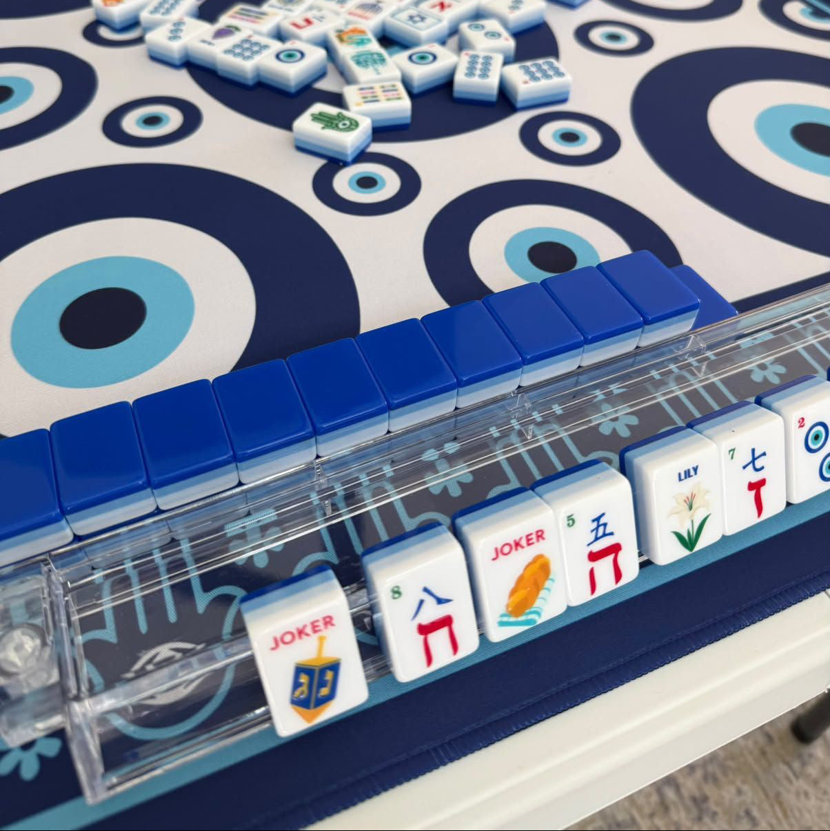 Shalom mahjong tiles on clear racks over the evil eye mahjong mat — the Shalom Mahjong Holiday Set bundle