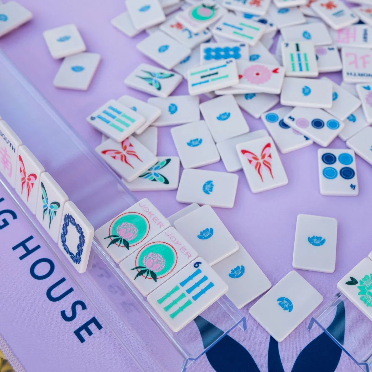 Lavender travel-size mahjong tiles scattered on a purple mat with a rack of jokers